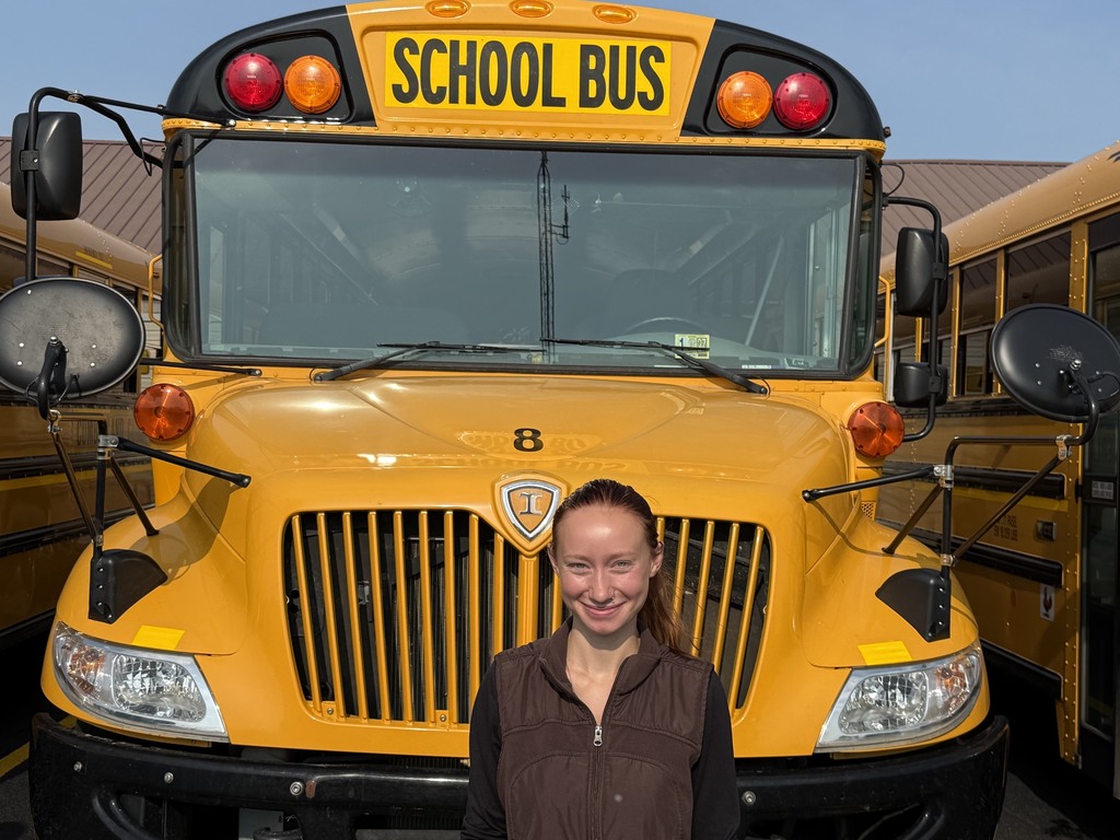 A bus driver is standing in front of their bus.