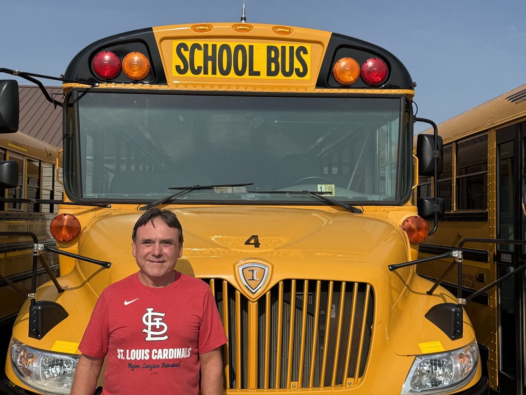 A bus driver is standing in front of their bus.