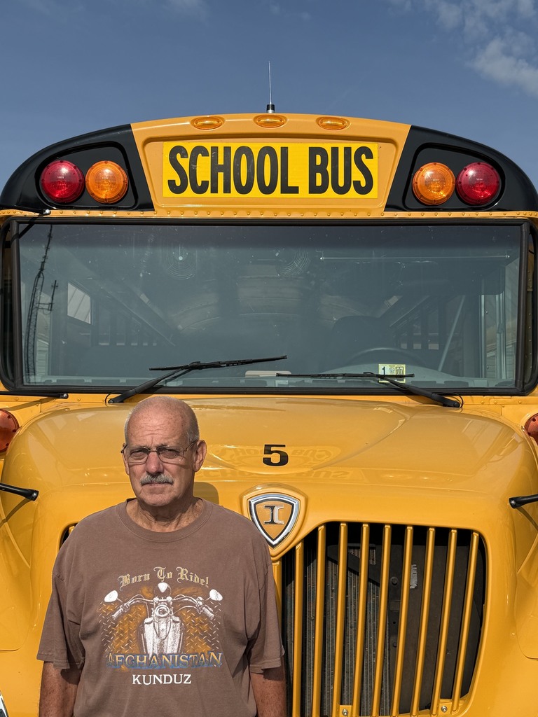 A bus driver is standing in front of their bus.