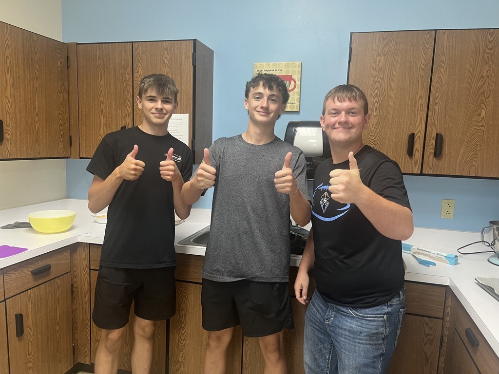 Three students are giving thumbs up in front of the kitchen counter. 