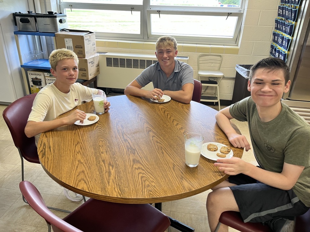 Three students are sitting at a table. Each has a plate of cookies and a glass of milk.