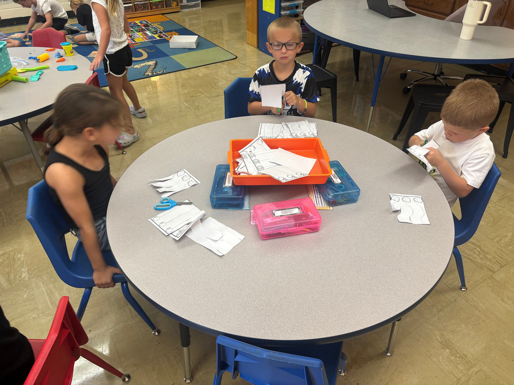 Three students are cutting paper at their table.