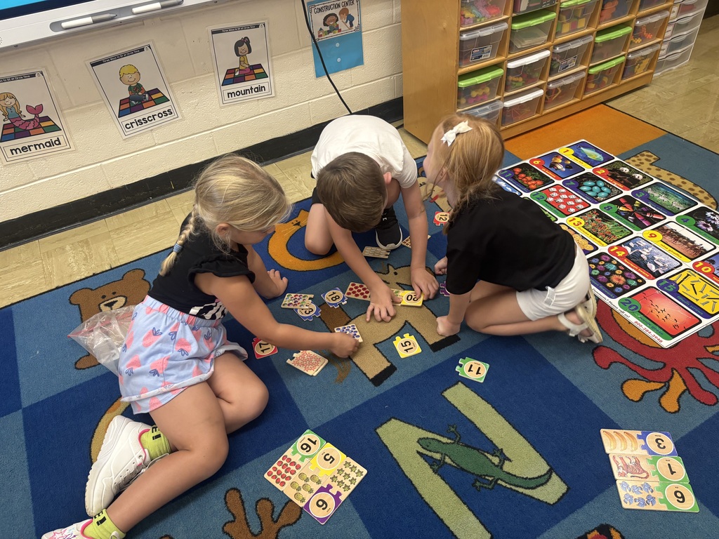 Three students are doing a puzzle on the classroom carpet.