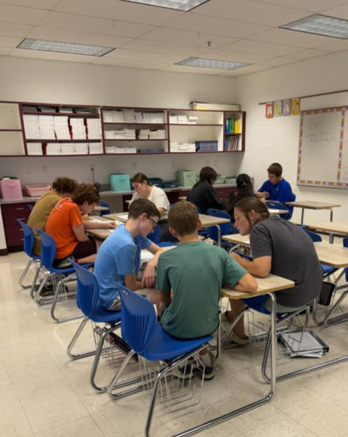 Students are working at their desks in groups to work out  problems to excape the room.