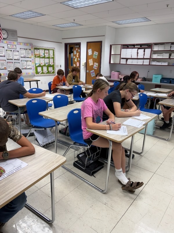 Students are working at their desks in groups to work out  problems to excape the room.