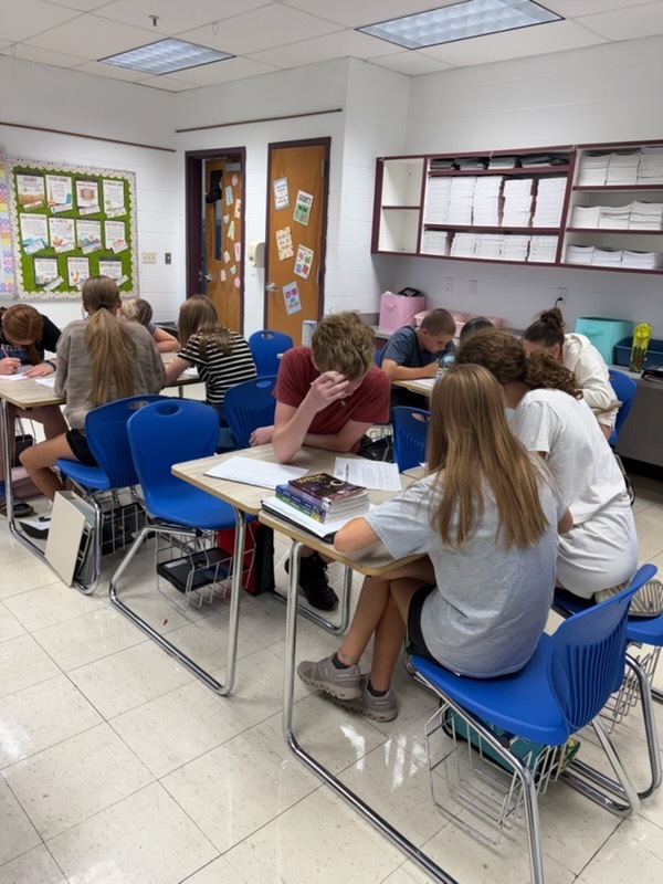 Students are working at their desks in groups to work out  problems to excape the room.
