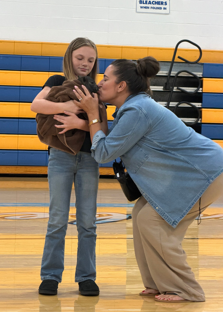 A student is holding a pig in a blanket. Mrs. McElravy is kissing the pig