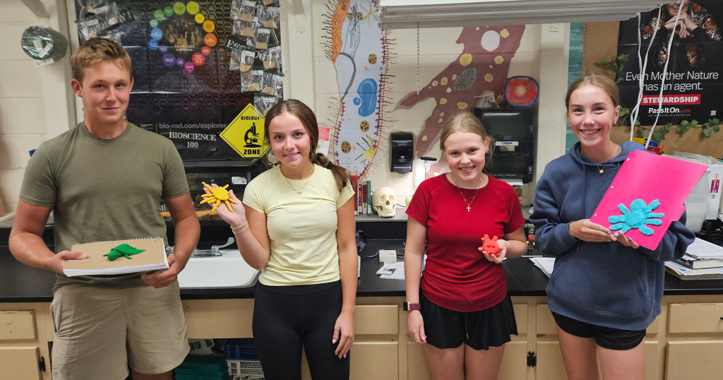 Students are standing side by side. Each is holding their symetrical animal made out of play-doh.