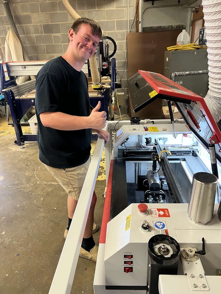 A student is standing in front of the engraving machine. He is giving thumbs up.