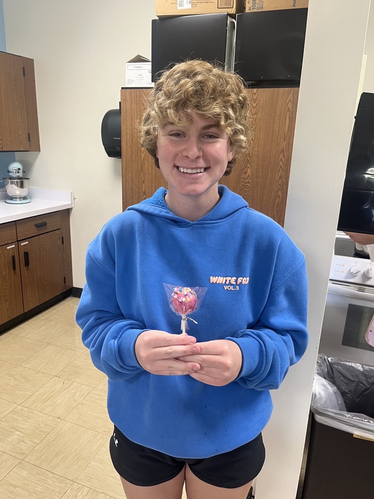 A student is holding a cake pop that has been wrapped in cellophane. 