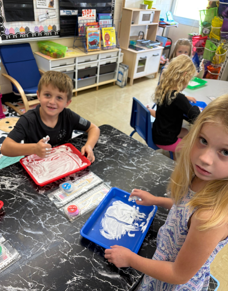 Two students are writing numbers on trays filled with shaving cream.