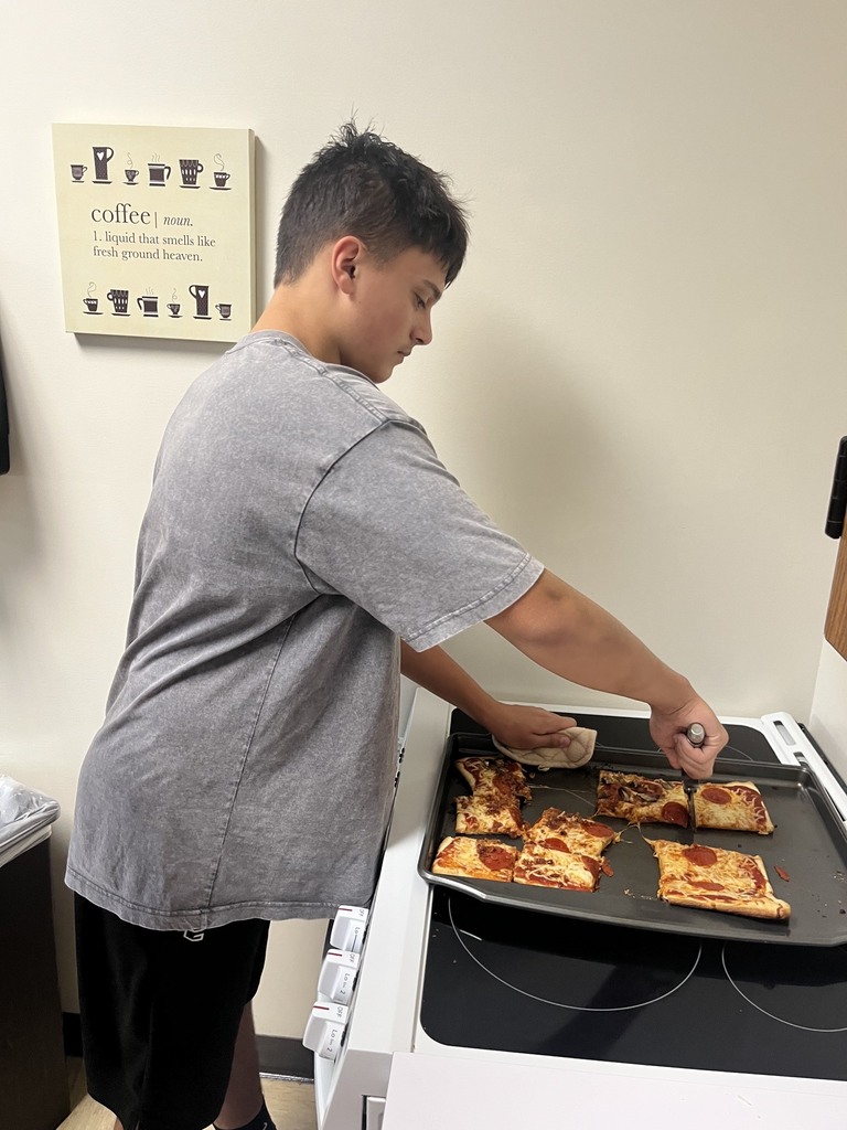 A student is cutting a piece of pizza from a baking pan.