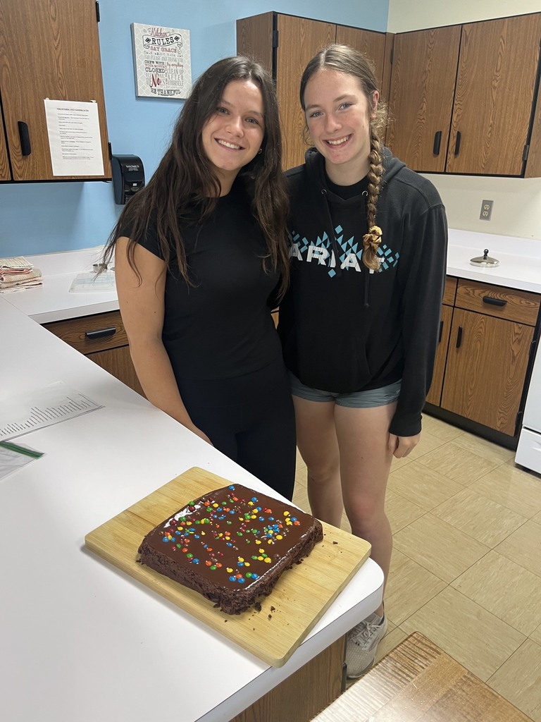 Two students are standing together. Their brownies are on a cutting board on the counter. 