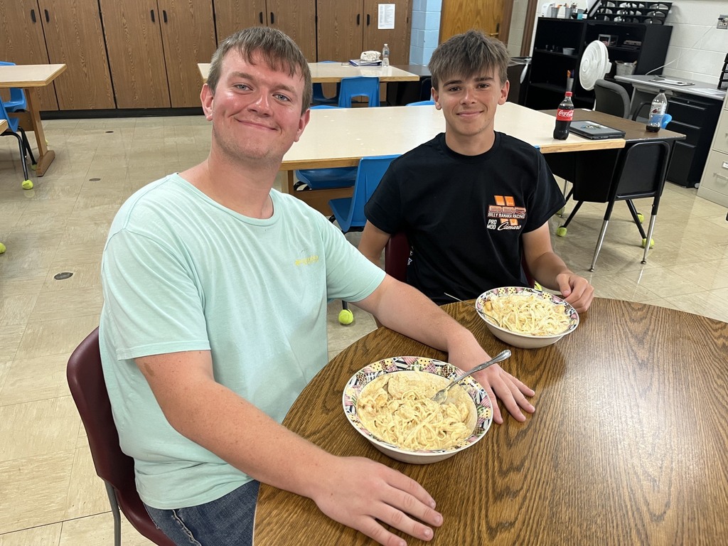 Two students are sittingtogether. Their bowls of chicken alfredo are setting in front of them.