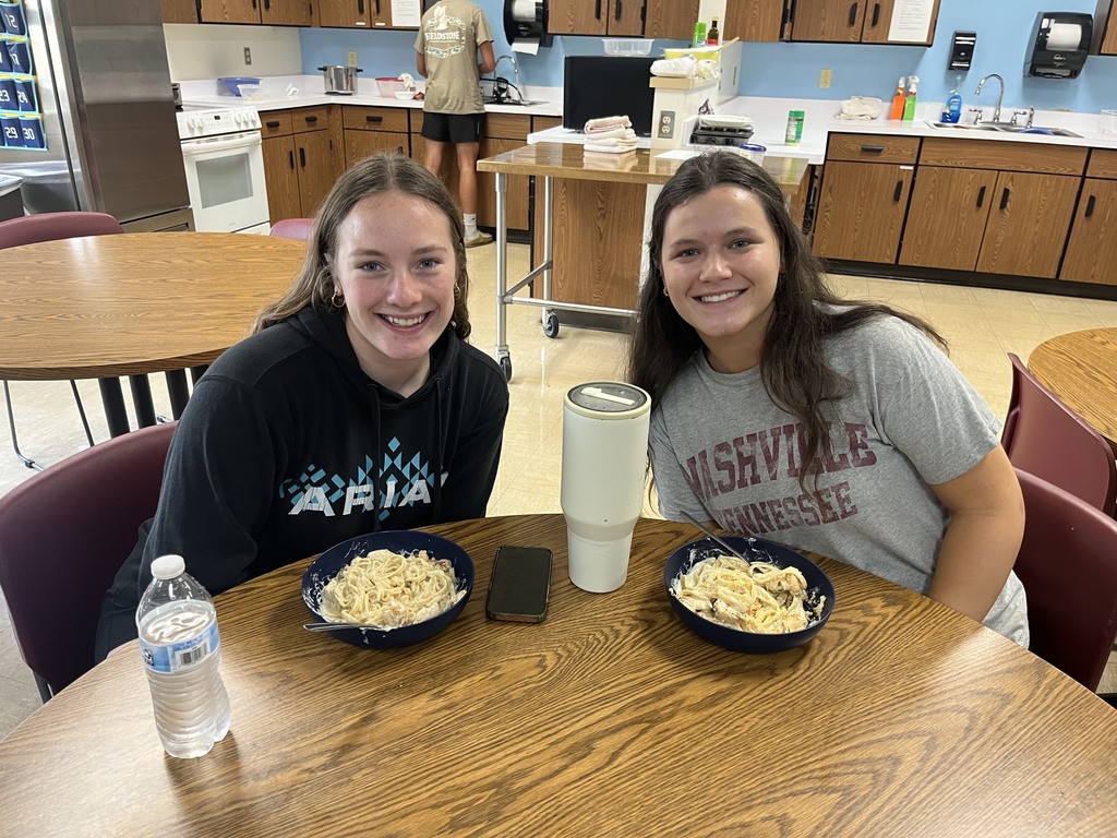 Two students are sittingtogether. Their bowls of chicken alfredo are setting in front of them.