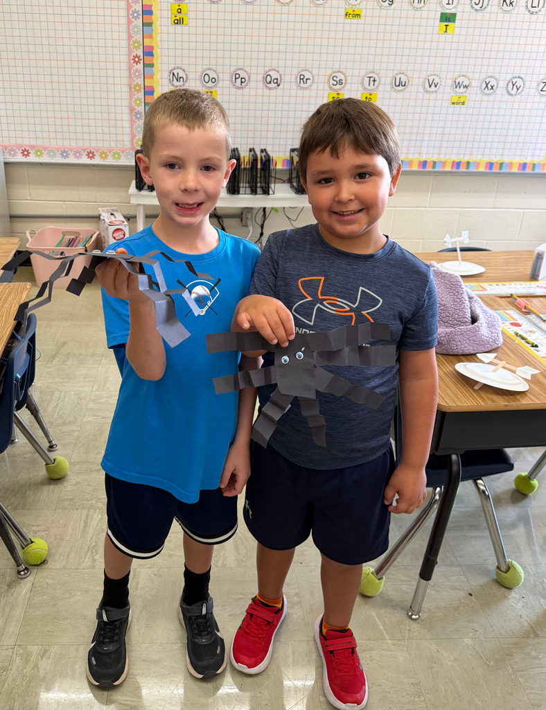 Two students are standing side by side. They are holding the spider they made.