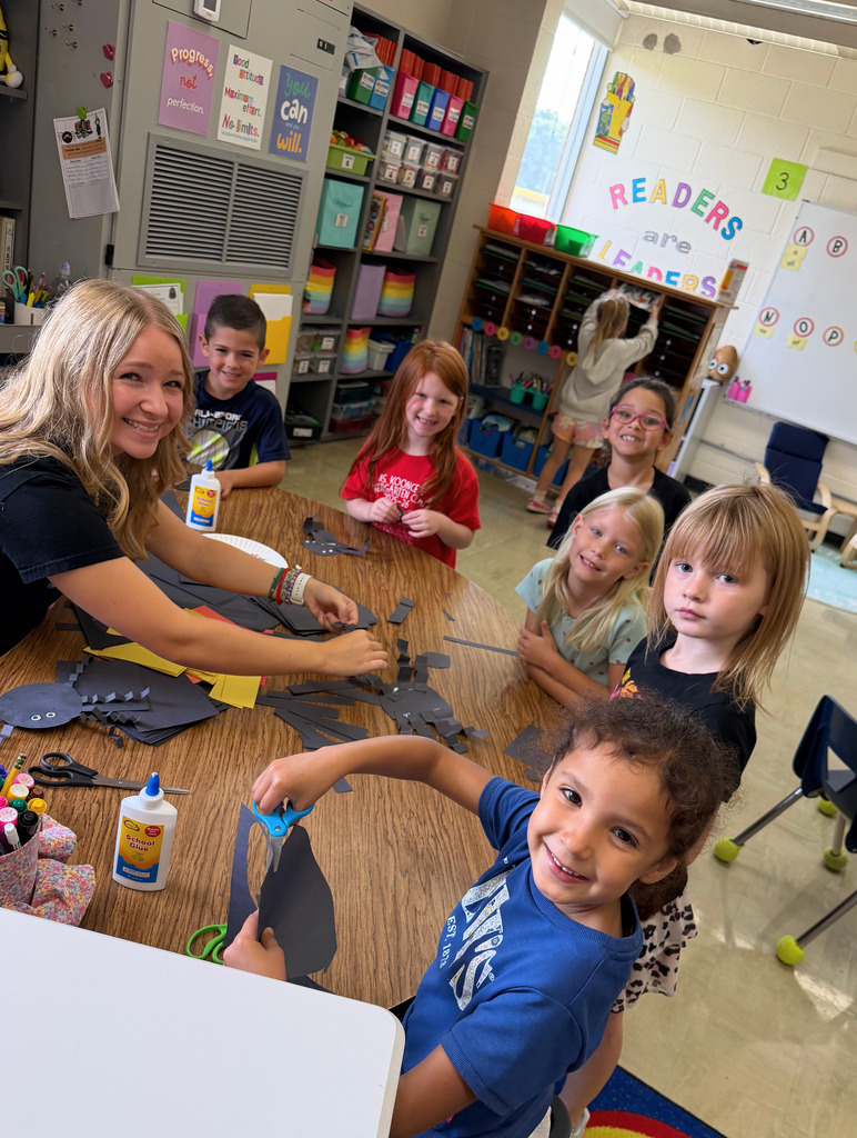 Six students and a teacher are crafting spiders at a table.