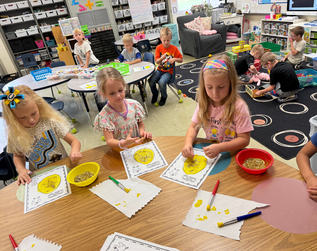Three students are painting a goose egg yellow at a table. 