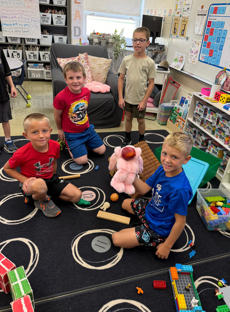 Four students are sitting at the carpet. They have a pink puppet.