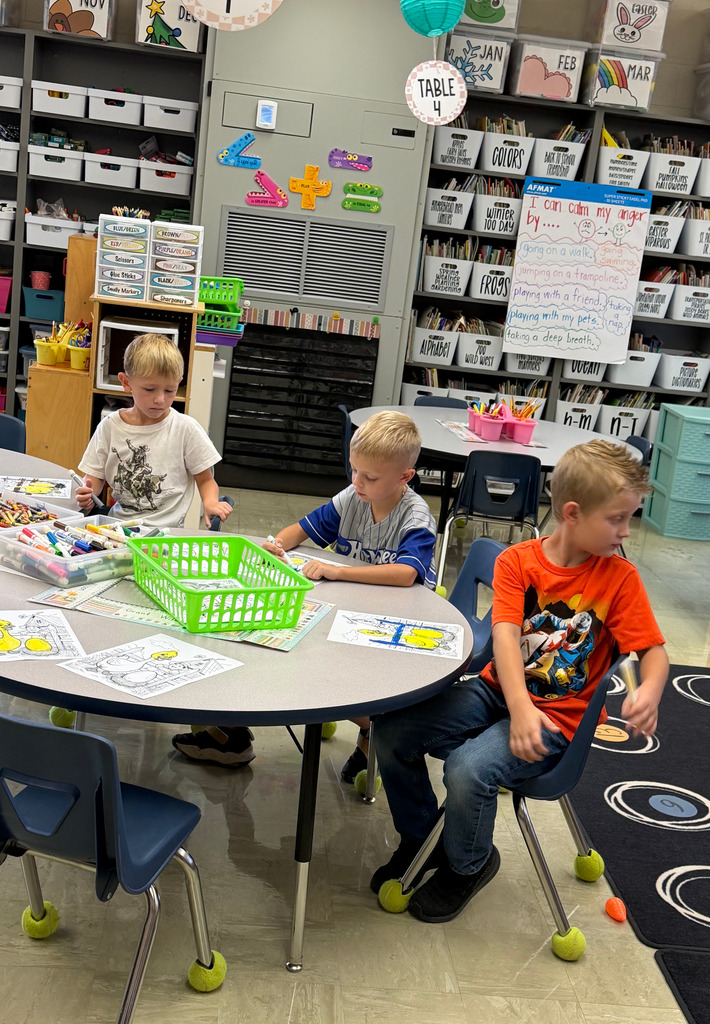 Three students are coloring a goose egg yellow at a table.