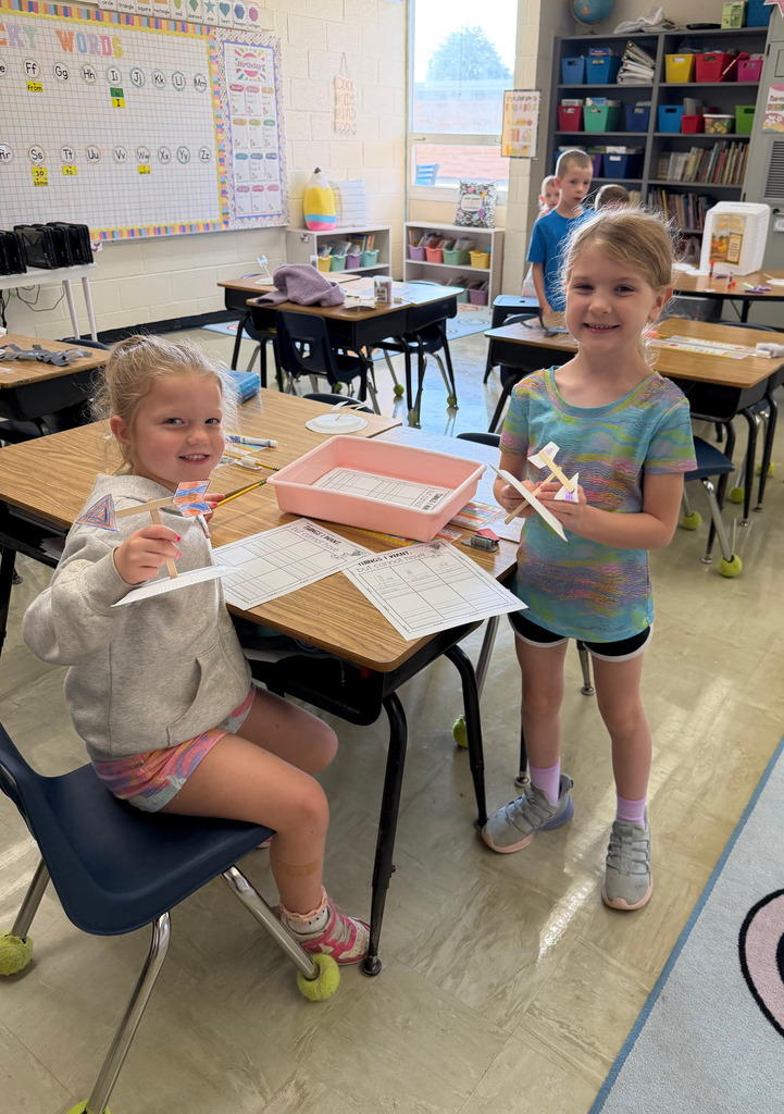 Two students are making a weather crane at a desk.