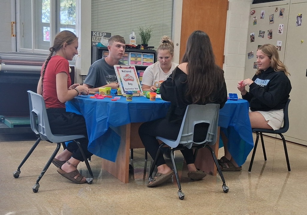 Five students are sitting at a table playing with Play-Doh. 