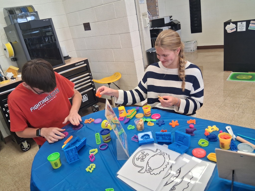 Two students are sitting at a table playing with Play-Doh. 