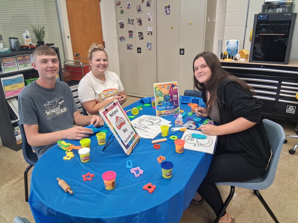 Three students are sitting at a table playing with Play-Doh. 