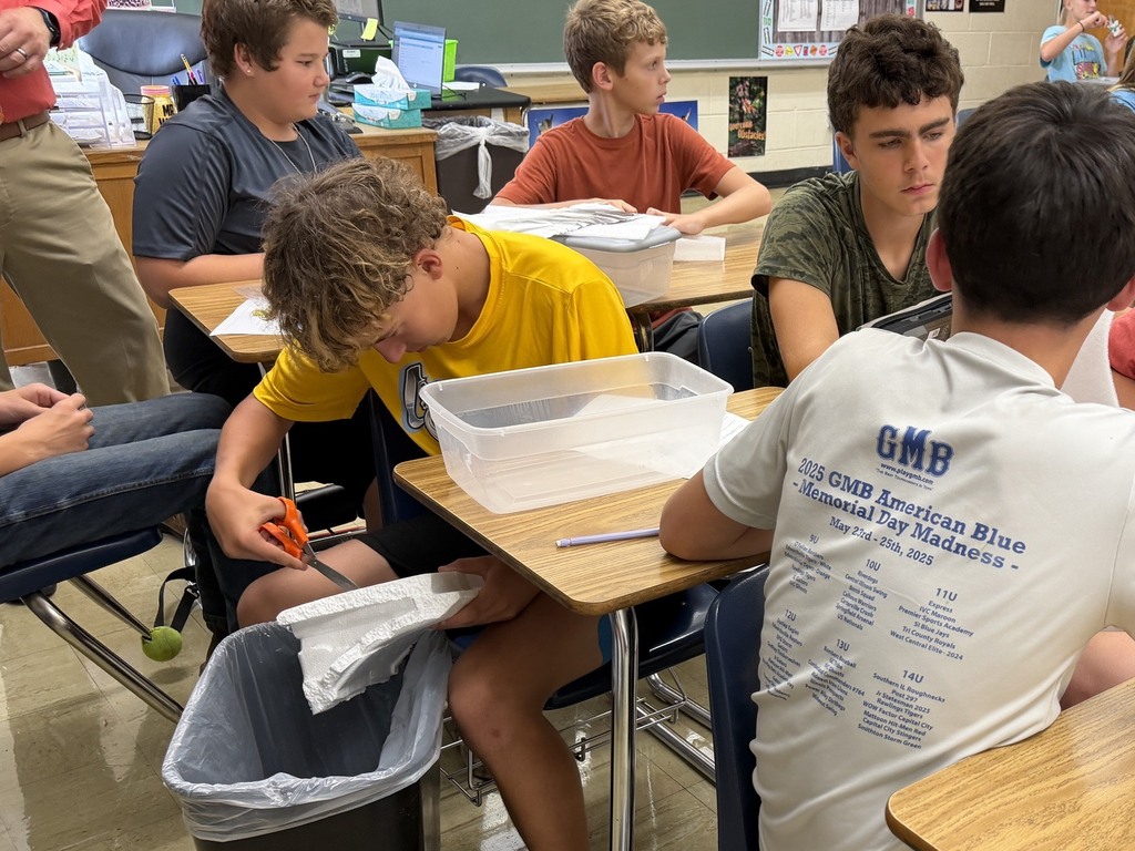 One student is cutting styrofoam. Two students are watching.