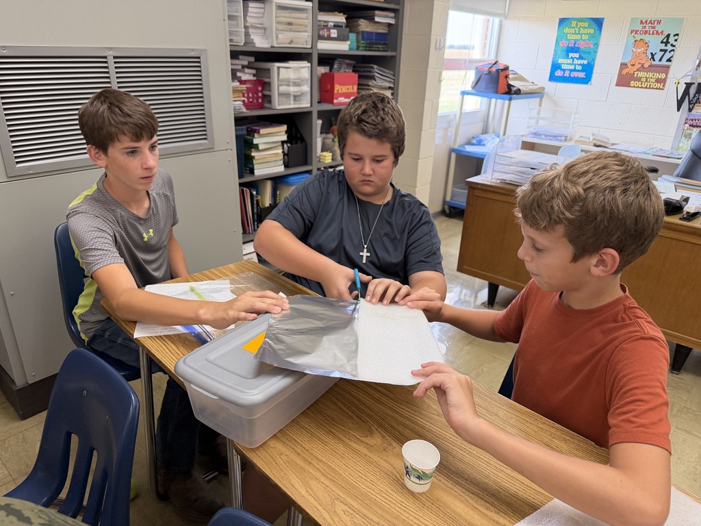 One student is cutting aluminum foil. Two students are holding it still.
