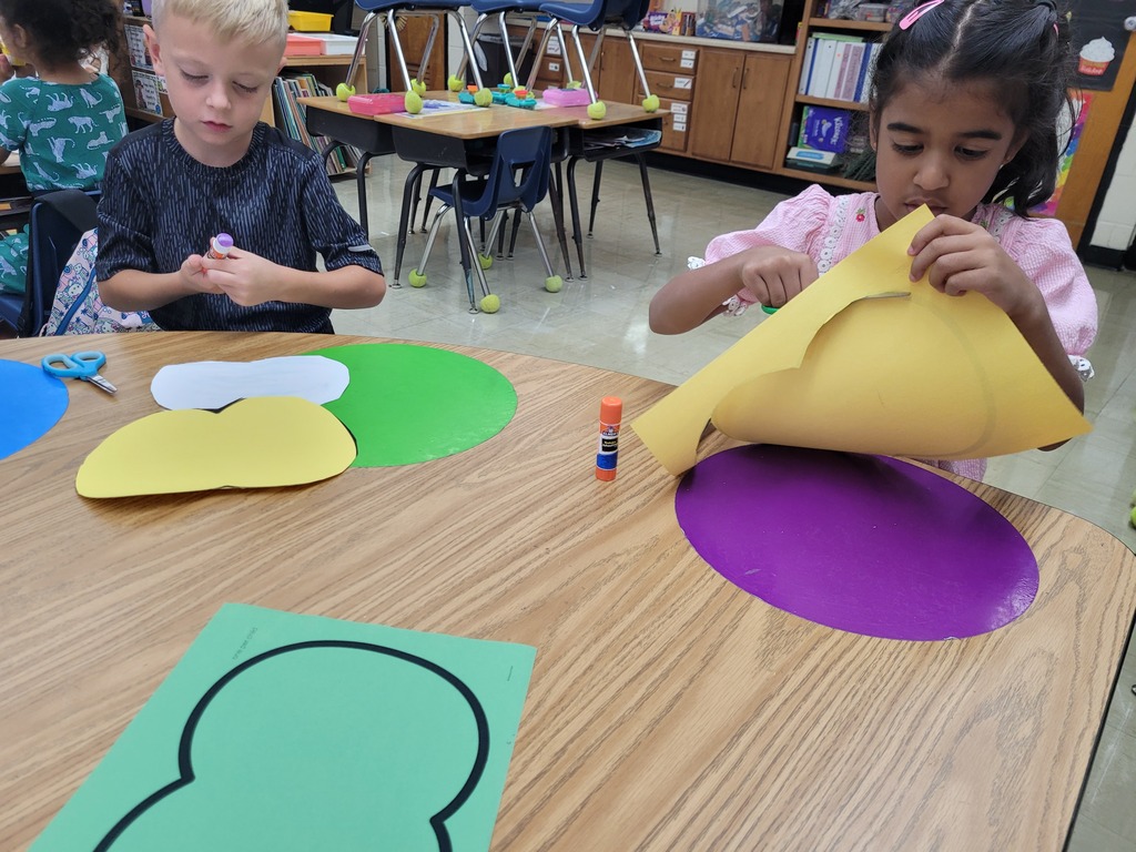 One student is cutting an apple shape and another is gluing apple parts together. 