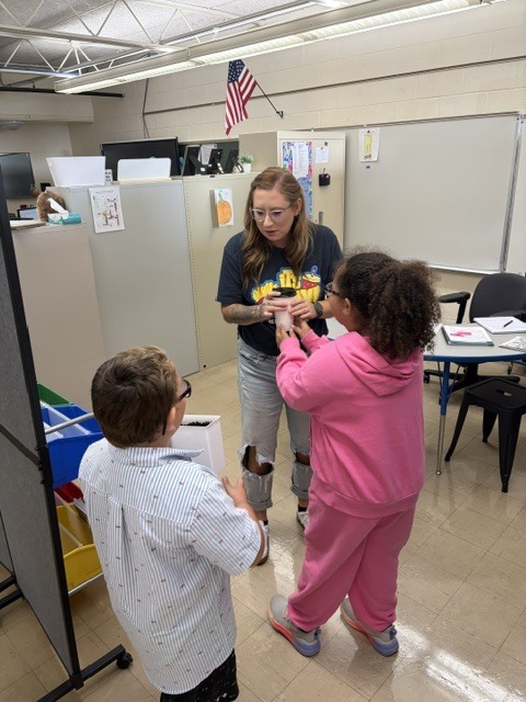 Twp students are delivering a cup of coffee to a teacher. 