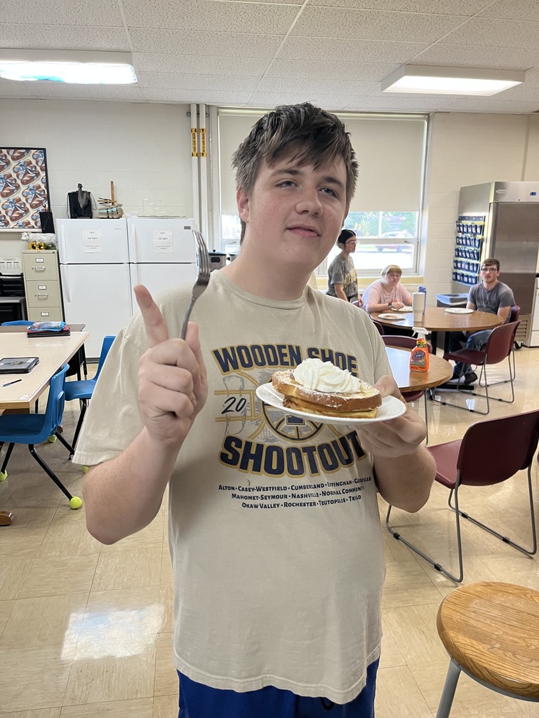 A student is holding a plate of French toast and is looking away with a hand point to the sky.