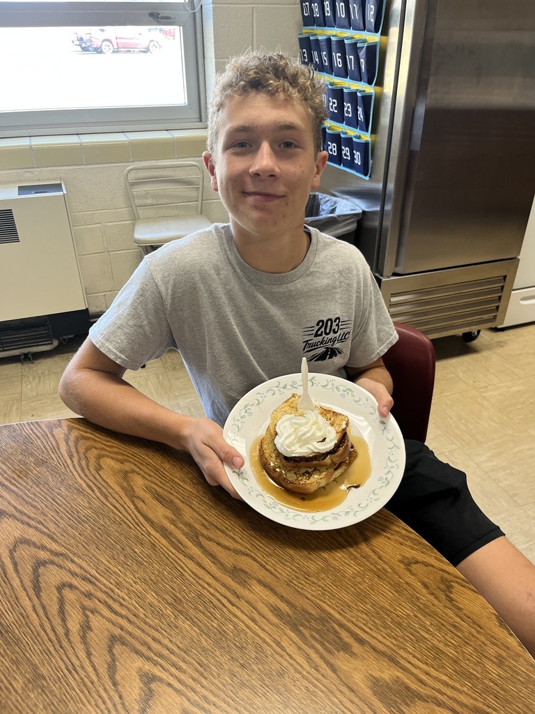 A student is sitting with a plate of French toast with syrup and whipped cream.