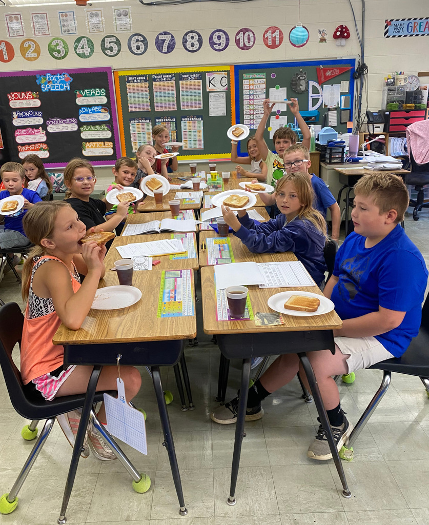 Students are sitting at their desks with plates of toast and drinks of tea.
