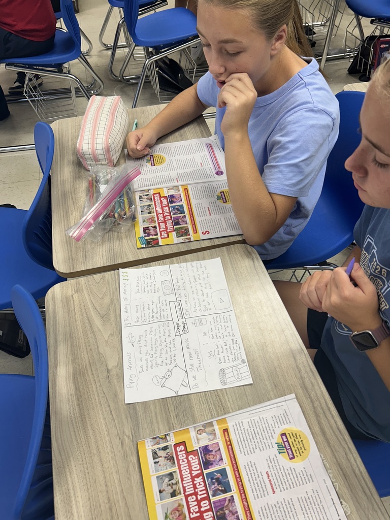 Students are sitting at desks discussing information from articles in the magazine. 