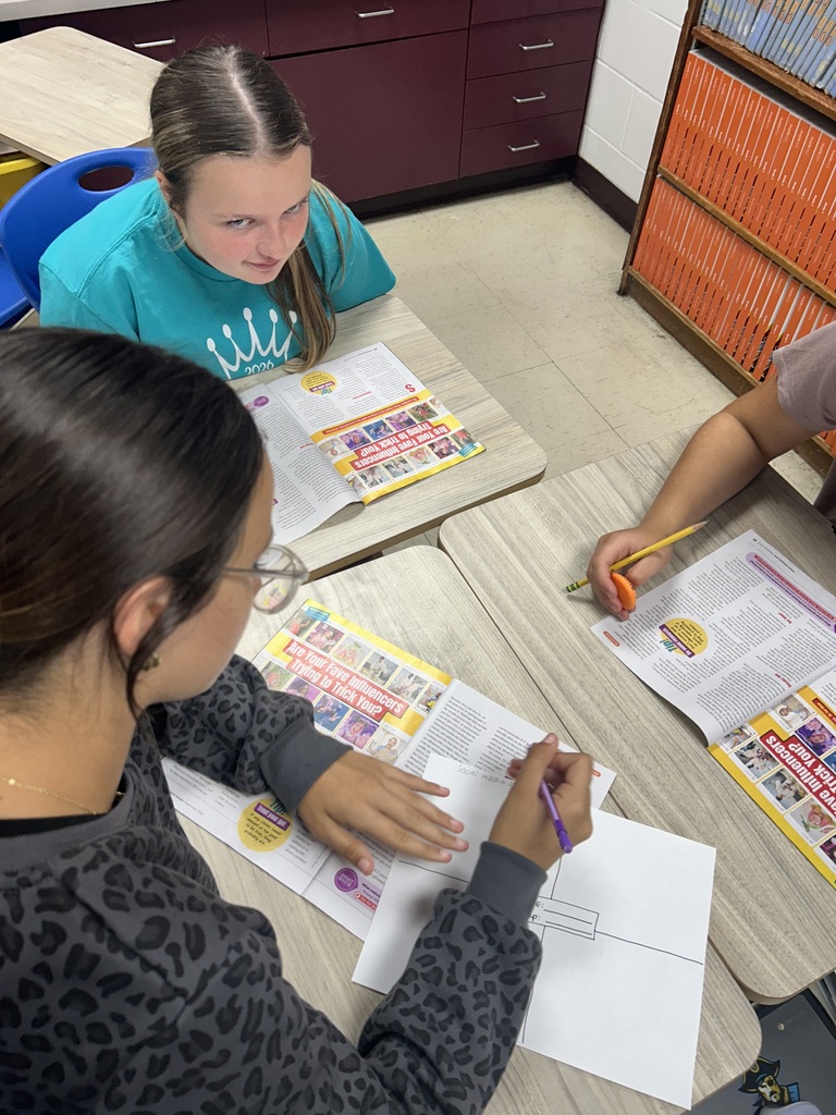 Students are sitting at desks discussing information from articles in the magazine. 