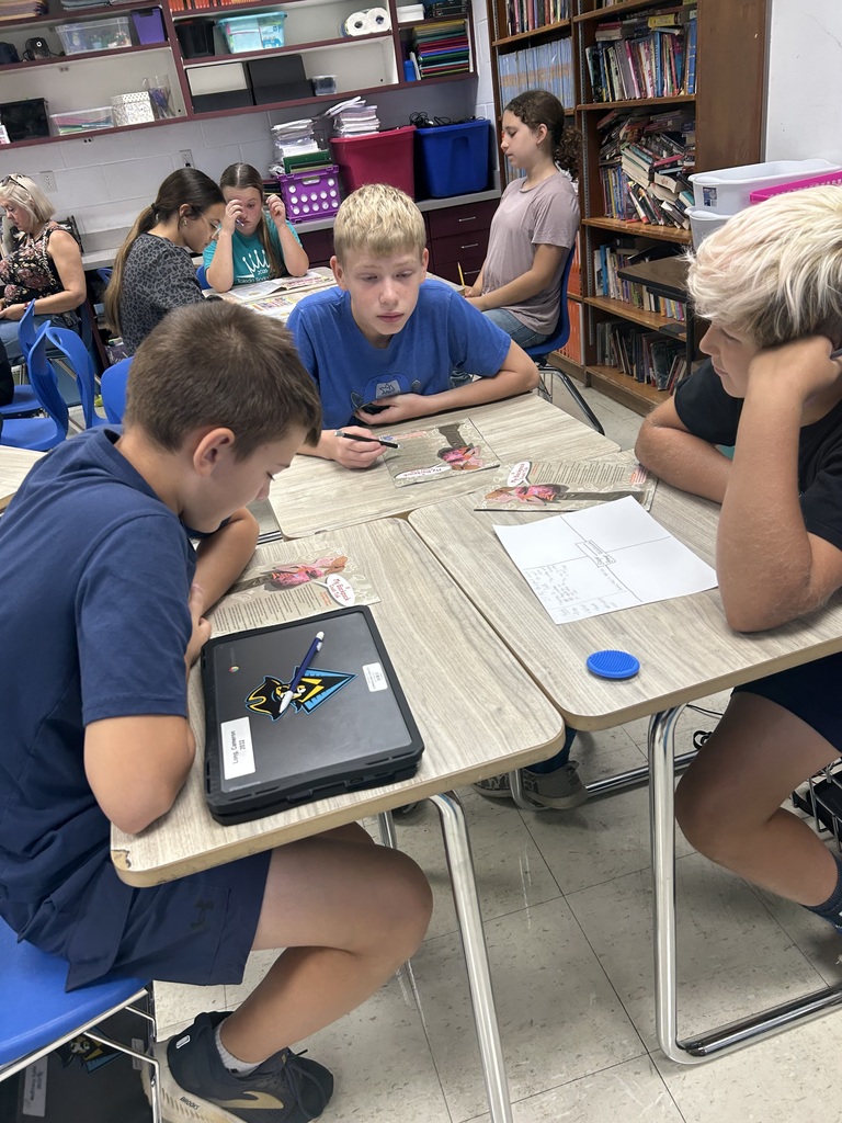 Students are sitting at desks discussing information from articles in the magazine. 