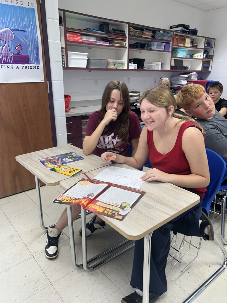 Students are sitting at desks discussing information from articles in the magazine. 