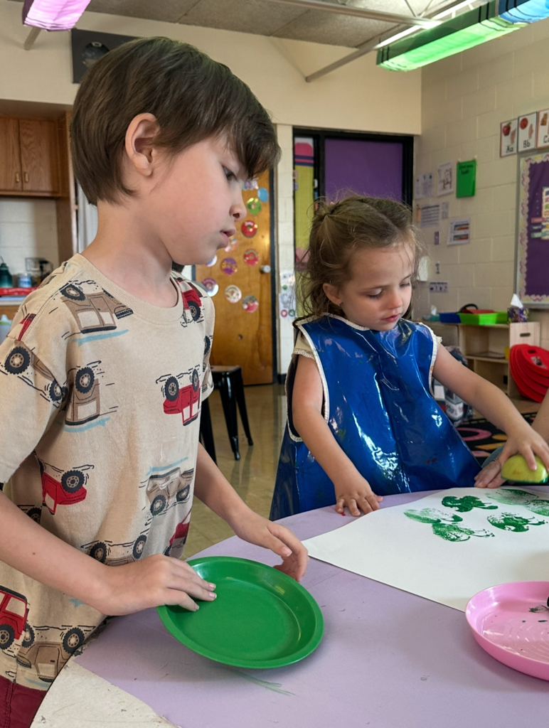 A student is stamping an apple on paper. Another student is watching.