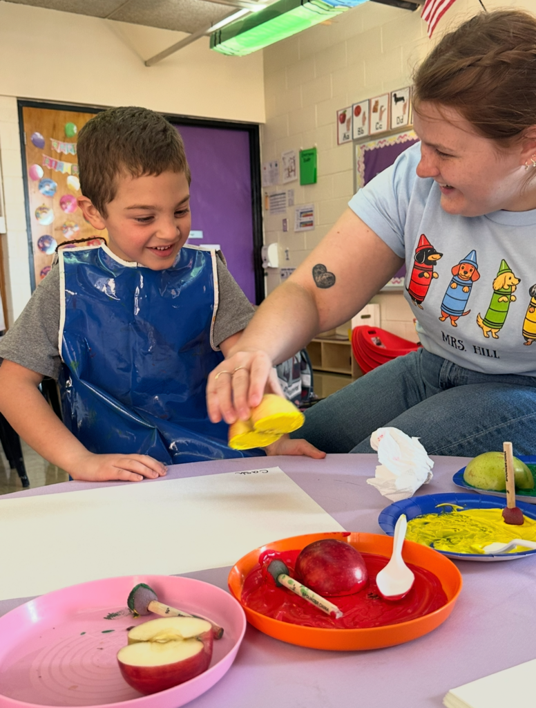 A stidemt os stamping an apple. The teacher is helping. 