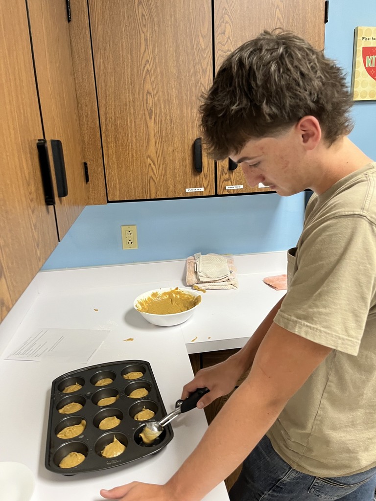 A student is dipping batter into a cupcake pan.
