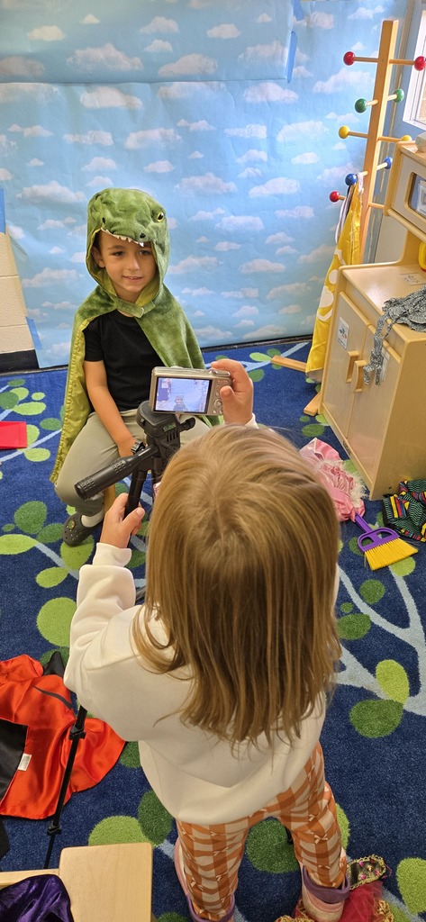 A student is taking a picture of another student wearing a dinosaur costume. 