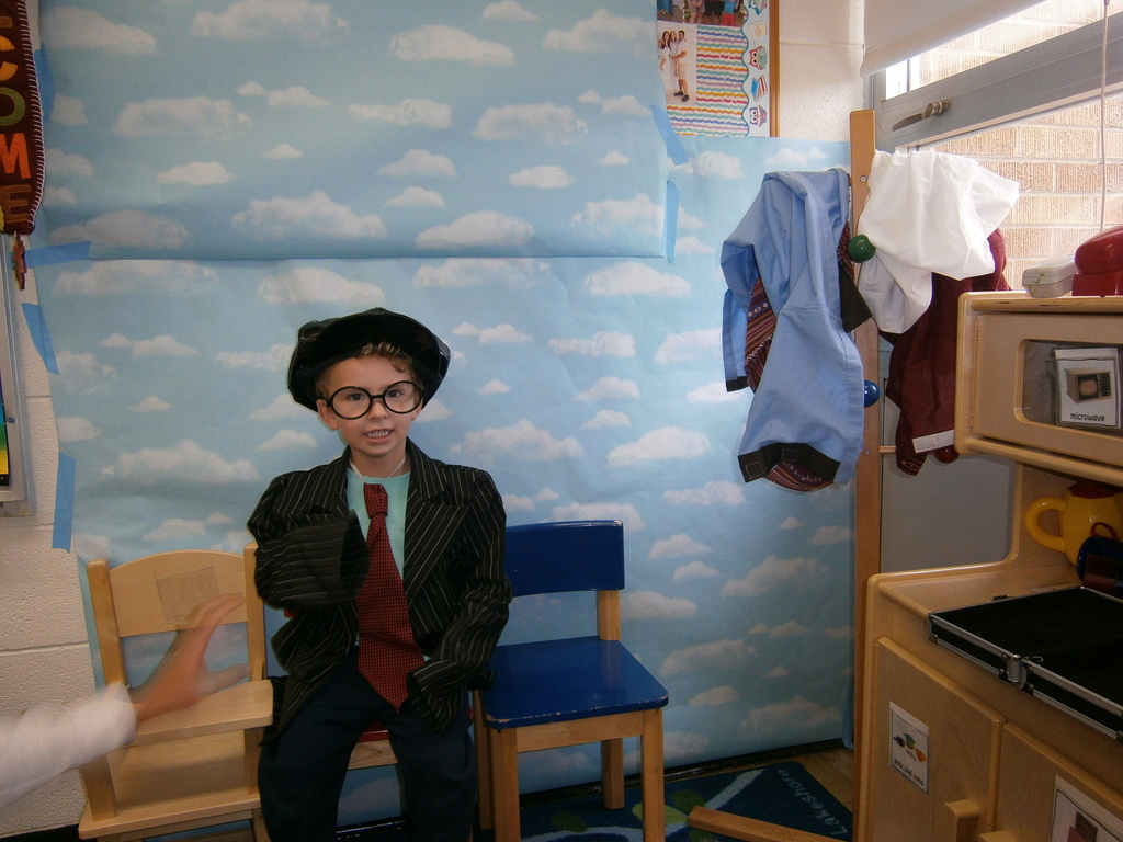 A student is getting their picture taken. The student is wearing a jacket and tie and a hat. 