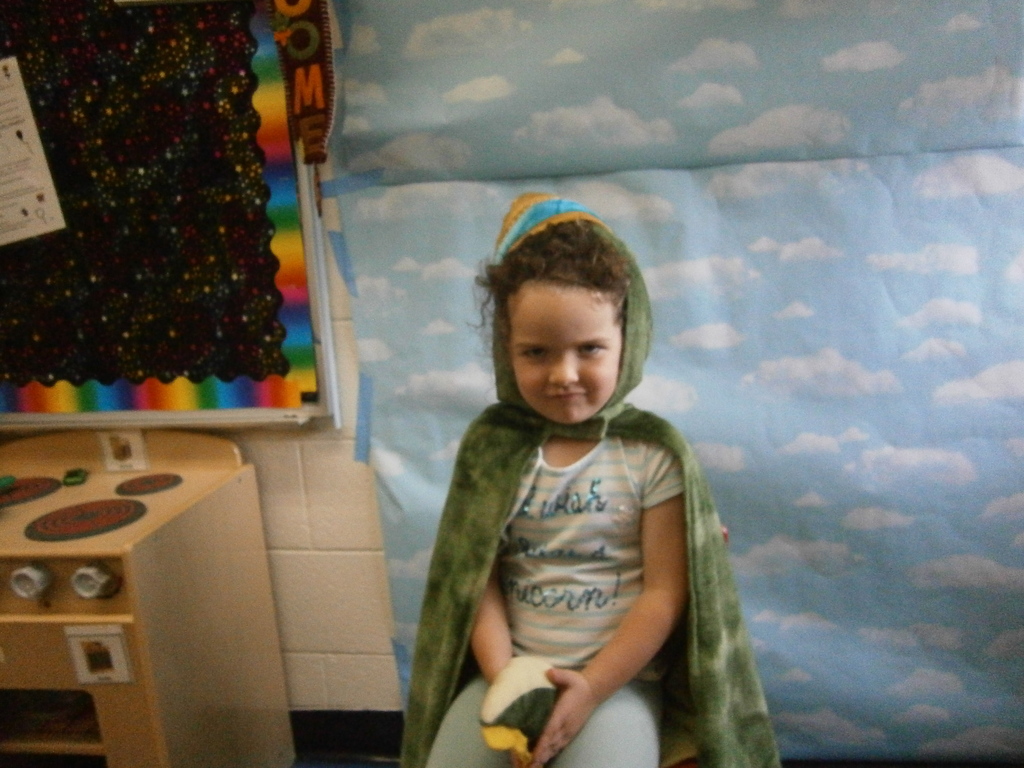 A studetn is wearing a green cape and a hat. 
