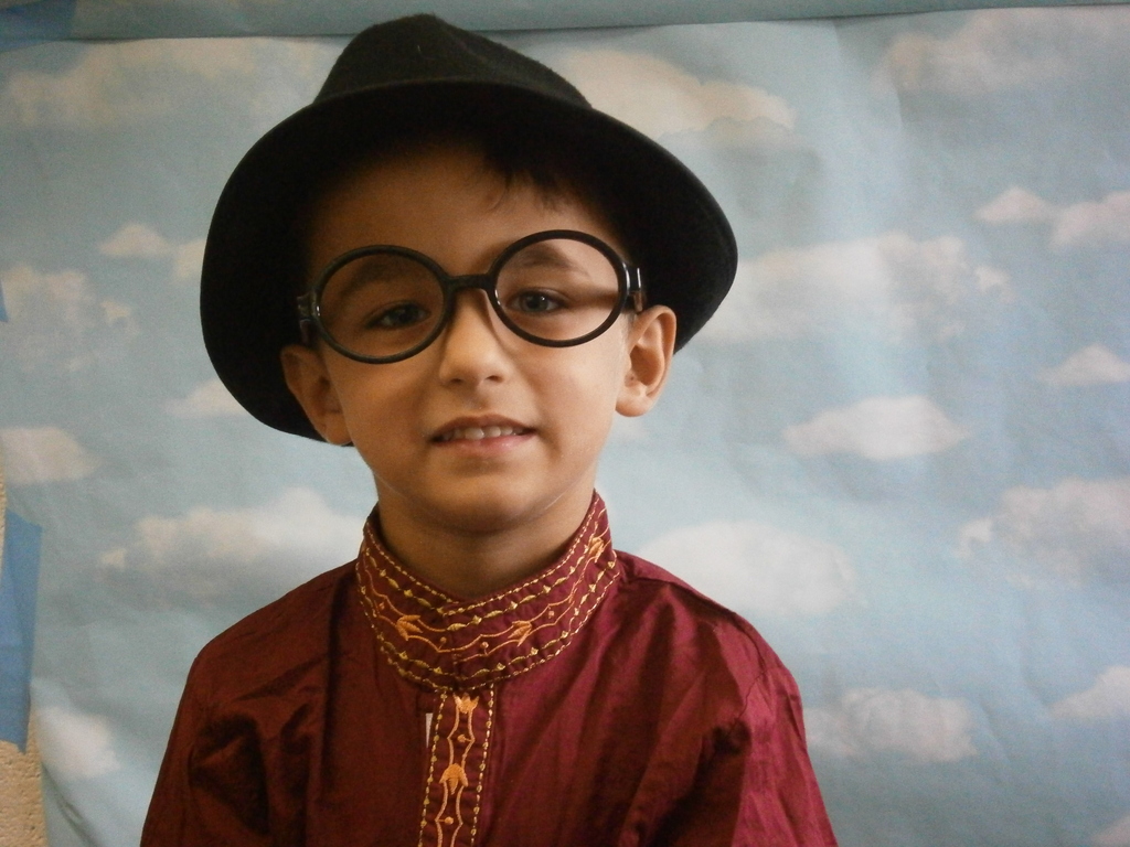 A student is wearing a hat, glasses, and red shirt. 