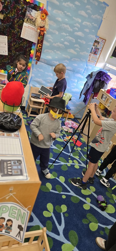 A student is setting up to take a picture. Two students are working in the background. A student has a hat and mask on. 