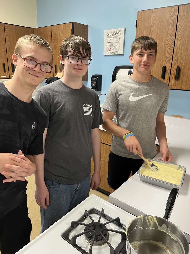 Three students are standing by a pan of mac and cheese. 