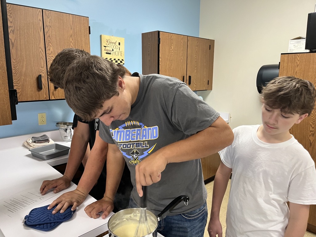 Three students are standing by a pan of mac and cheese. 