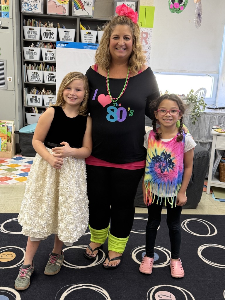 Two students and a teacher are dressed in decade-themed outfits. 